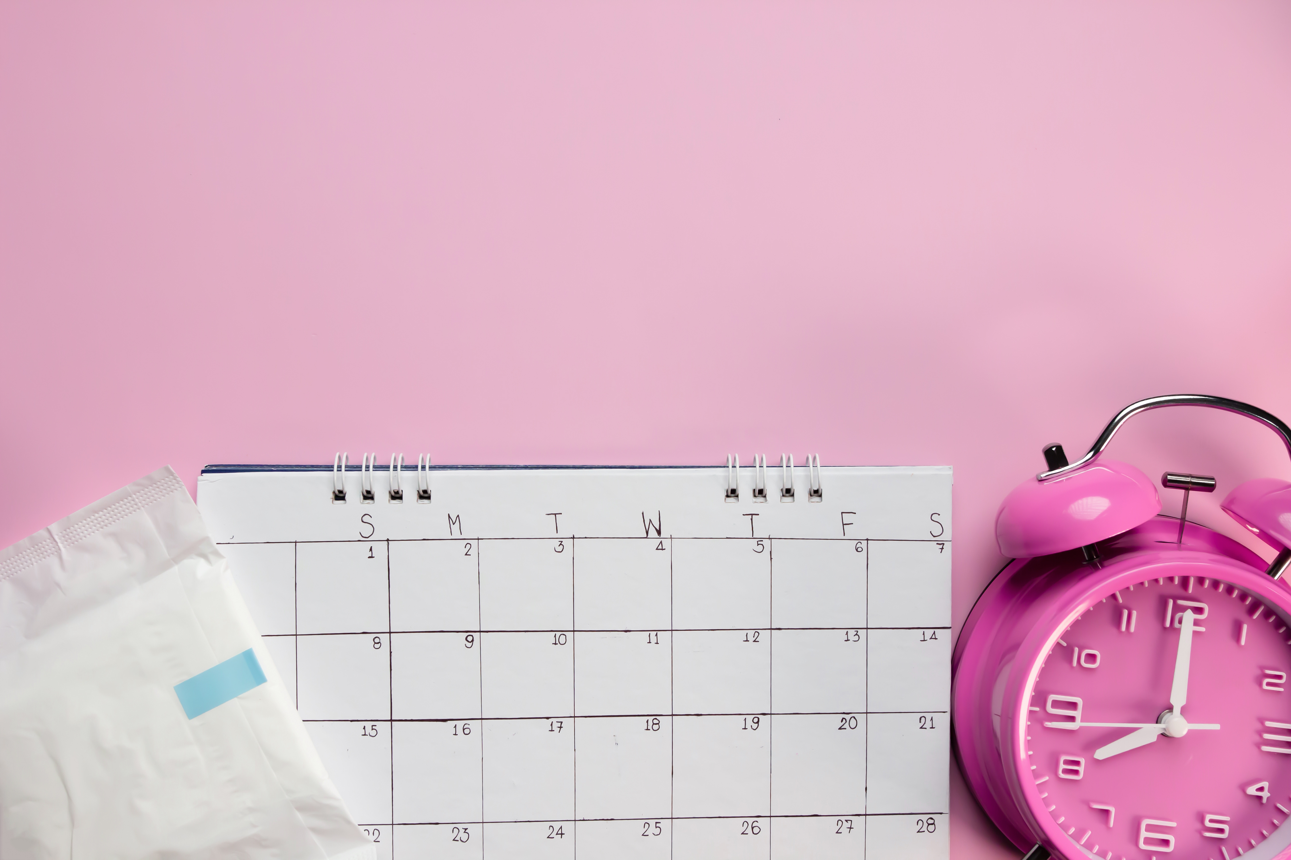 a sanitary towel, empty calendar and alarm clock on a pale pink background.