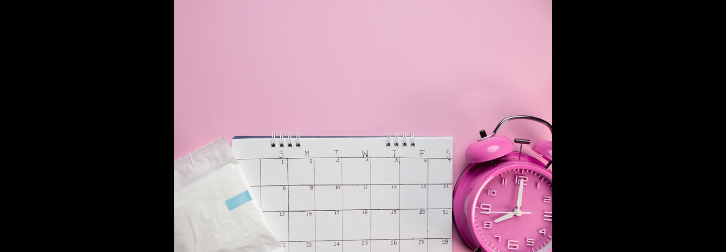 a sanitary towel, empty calendar and alarm clock on a pale pink background.