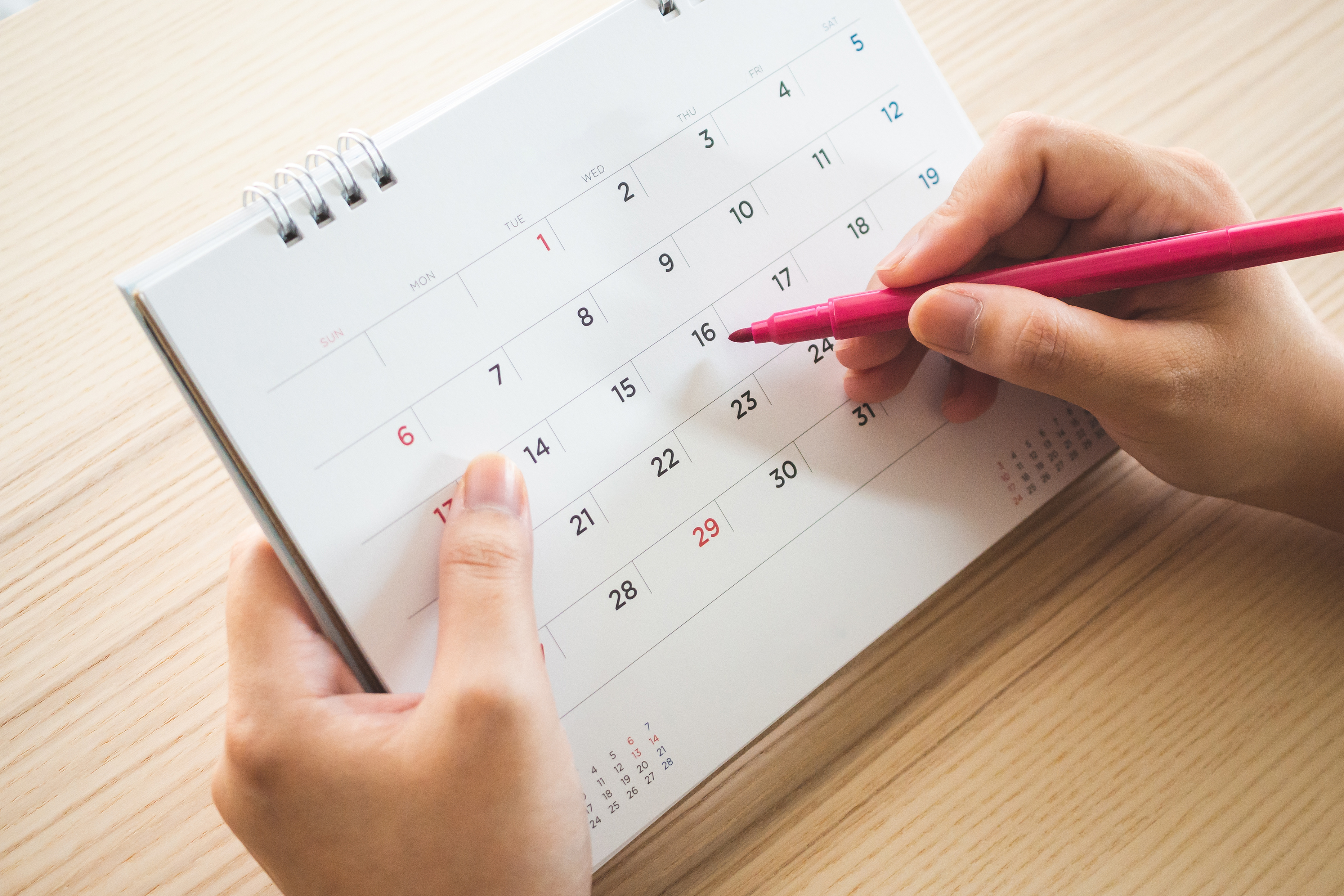 A woman holds a pen and a blank calendar, ready to mark on her expected period date.