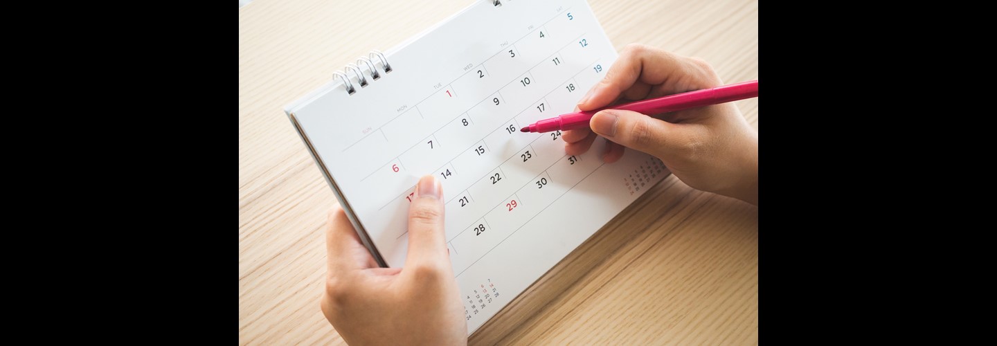 A woman holds a pen and a blank calendar, ready to mark on her expected period date.