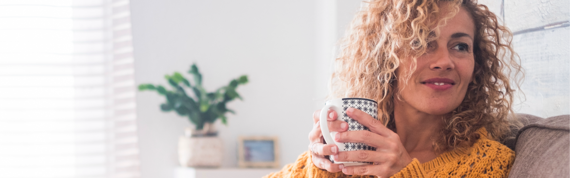 Woman in a yellow jumper sat on a chair drinking a hot drink