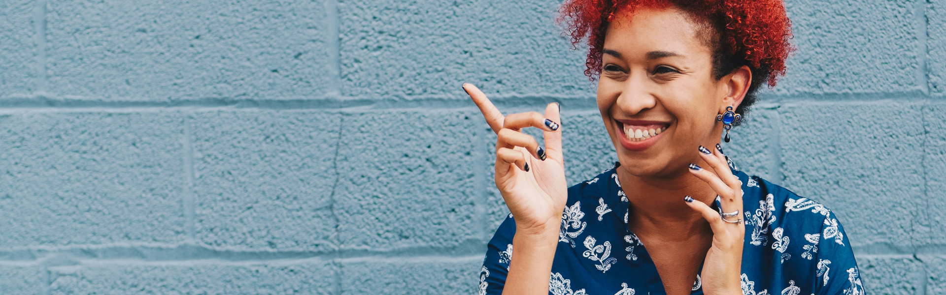 Lady stood in front of a blue painted brick wall wearing a blue shirt, smiling