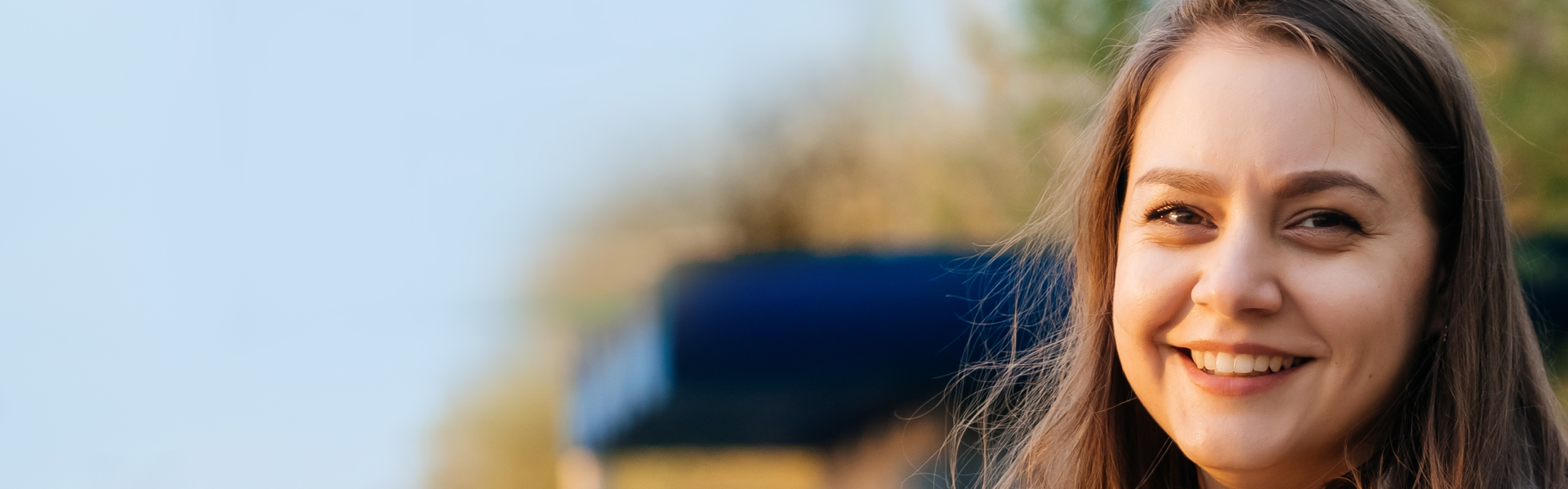 Woman in the outdoors with her hair blowing in the wind, looking at the camera and smiling