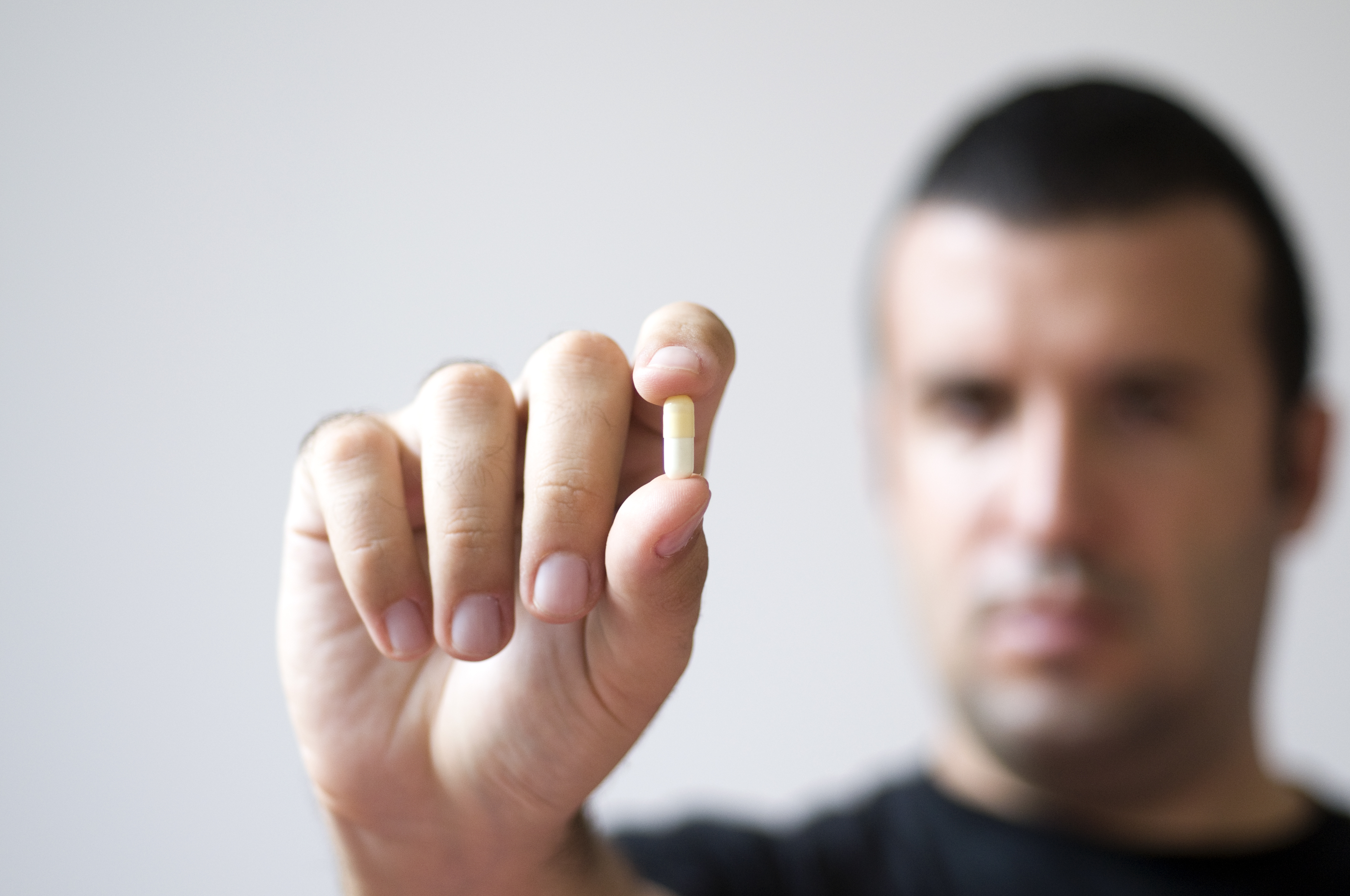 a man holding up a small white capsule in his hand